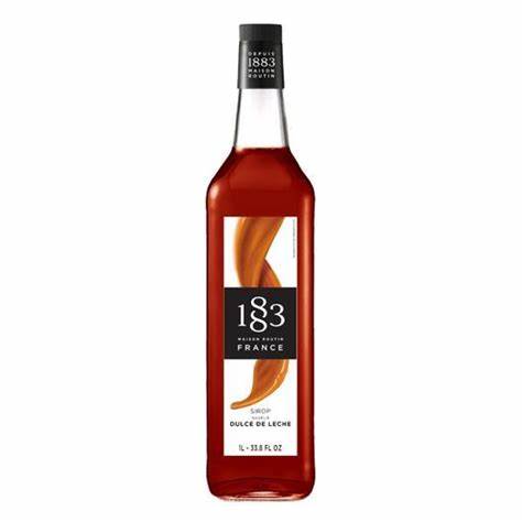a glass 1883 bottle with warm brown syrup and a caramel ribbon running down the front with a black 1883 label on the front 