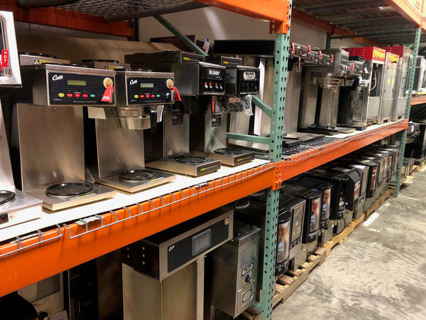 Pallet racking full of Curtis and Bunn coffee brewers that are reconditioned below them are some cappuccino machines and off to the right are coffee grinders and other coffee and espresso equipment and at the very end you will see popcorn machines 