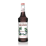 a glass bottle filled with deep purple blueberry syrup, a white label on the front with blueberry stems rising across the label with green leaves and fresh ripe blueberries