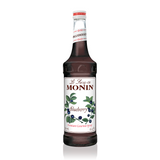 a glass bottle filled with deep purple blueberry syrup, a white label on the front with blueberry stems rising across the label with green leaves and fresh ripe blueberries