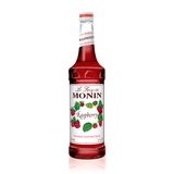 bright red syrup in a glass bottle with a white label  full of bright red raspberries and bright green raspberry leaves