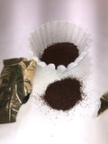 a gold empty packet of coffee on the left next for a small but neat pile off ground coffee and a coffee filter filled with ground coffee 