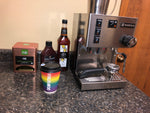 a Rancilio espresso machine set up in a small office building with some cups, syrups and condiments.